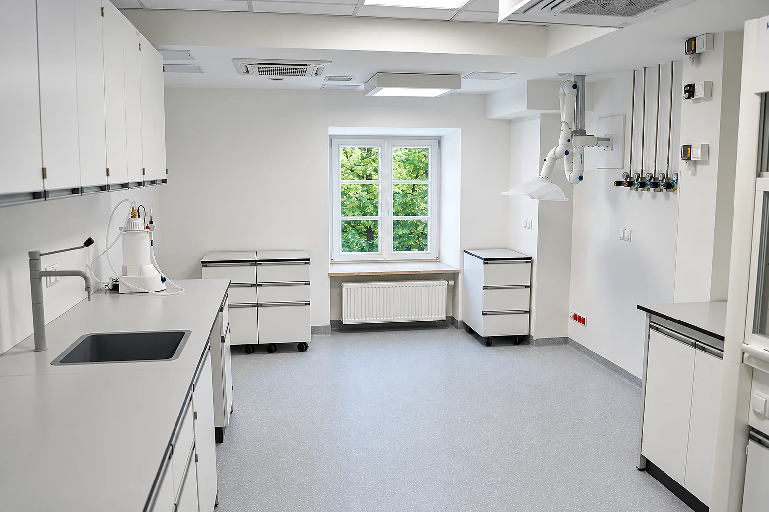 Laboratorium z meblami Renggli: stół ze zlewem, szafki wiszące, zawory gazowe i ramię odciągowe