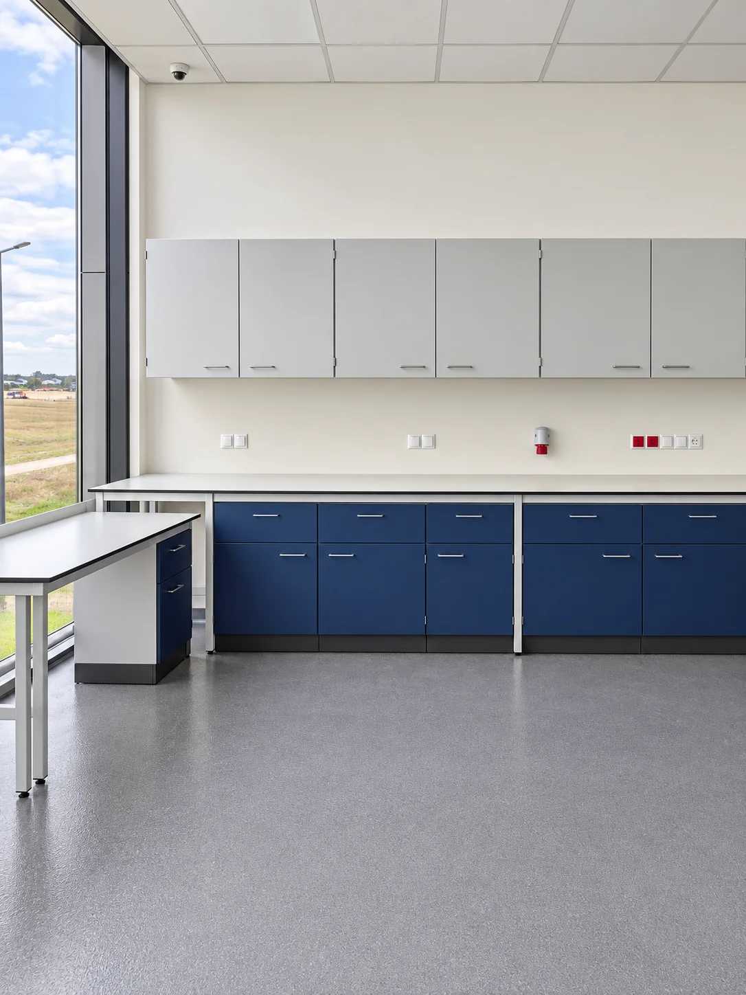 Laboratorium BART: granatowe szafki z szufladami pod jasnym blatem, szafki wiszące i stół przy przeszklonej ścianie